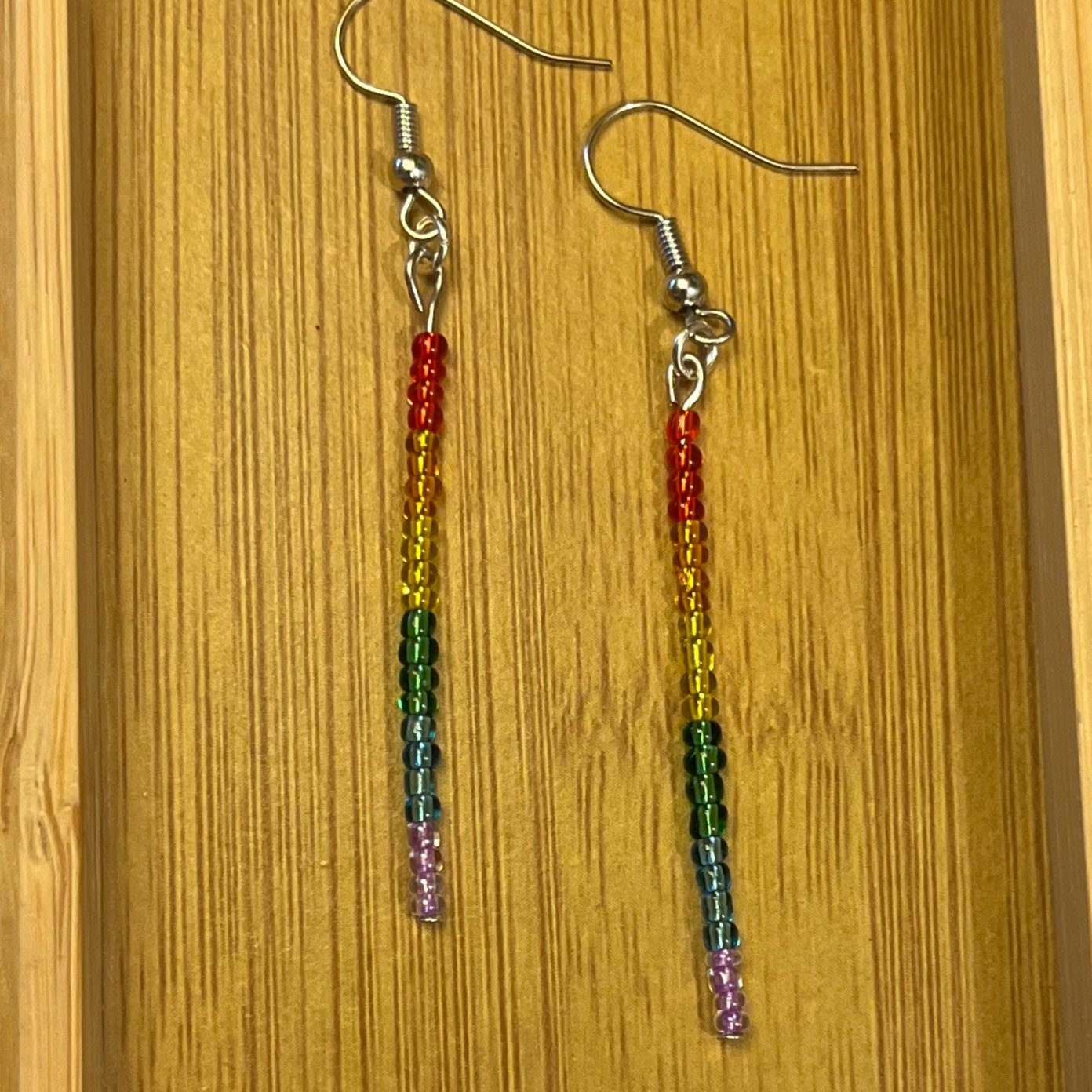 Pride stick earrings with the traditional rainbow colours in semi-transparent glass seed beads: red, orange, yellow, green, blue, purple.